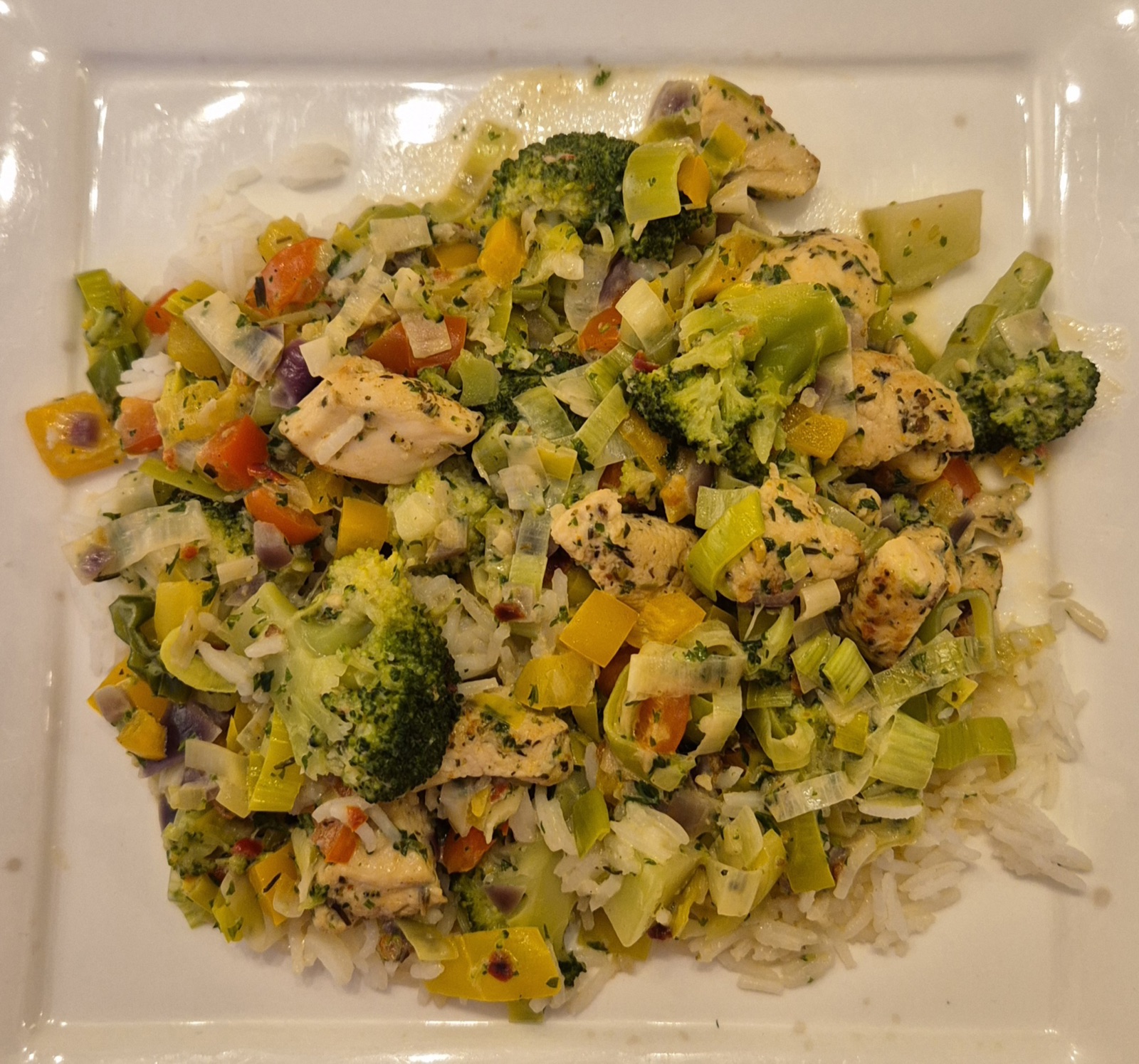 Een bord Provençaalse zomerkip met rijst, paprika, prei en broccoli.